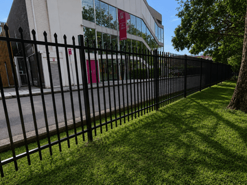 Matte black spear-top steel fencing along a commercial lawn beside a glass-fronted building.
