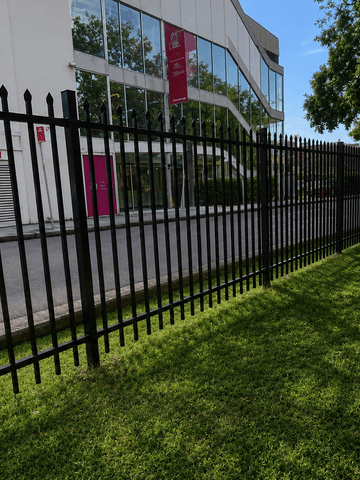 Matte black spear-top steel fencing along a commercial lawn beside a glass-fronted building.