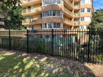 Stepped black spear-top panels following ground slope beside established trees.