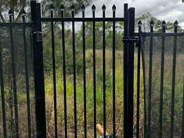 Olive-green spear-top tubular fence bordering a garden bed and pathway.
