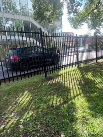 Spear-top steel boundary running behind large tree trunks on sloping ground.
