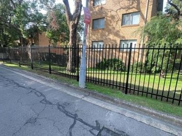 Spear-top panels along a brick apartment wall above garden mulch.