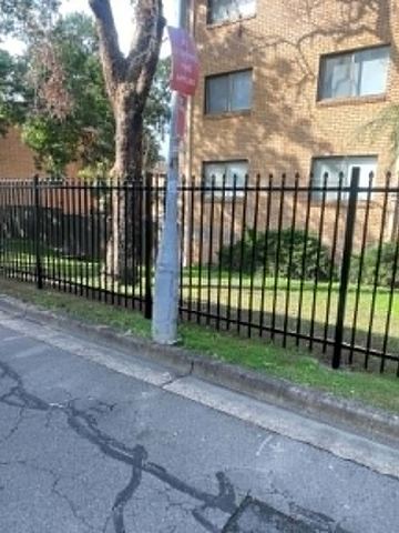 Spear-top panels along a brick apartment wall above garden mulch.