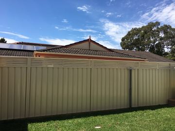 Cream slat-topped gate and panels span a green lawn before a brick house with solar panels on the roof.