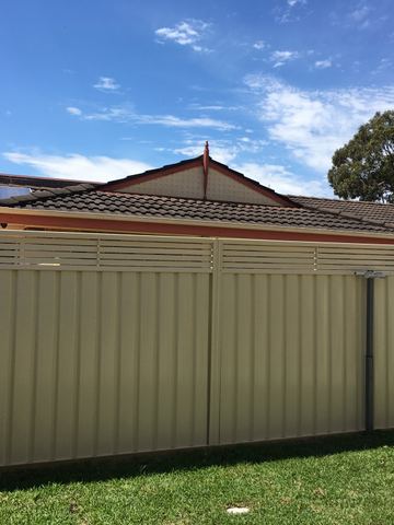 Cream slat-topped gate and panels span a green lawn before a brick house with solar panels on the roof.