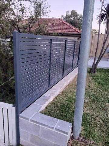 Horizontal aluminium slats mounted on a concrete block wall above a paved patio.