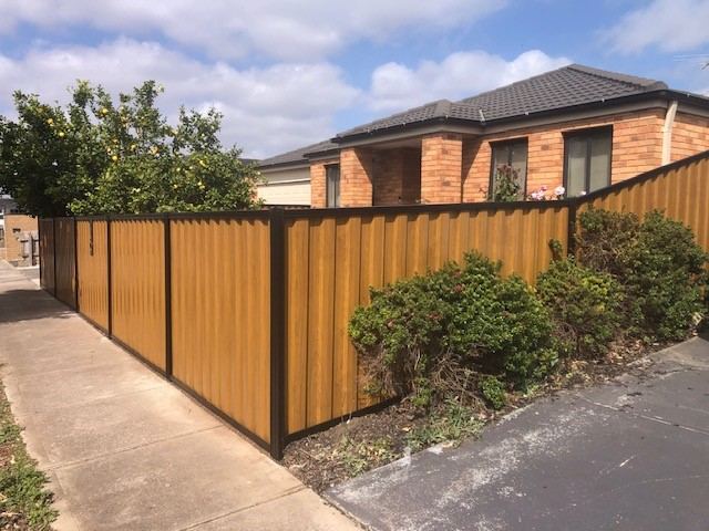 Light Oak woodgrain steel fence with black posts along a front boundary in front of a brick house