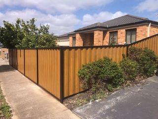 Light Oak woodgrain steel fence with black posts in front of a brick house