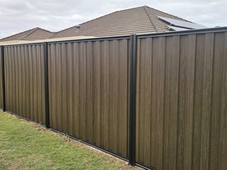 Installed Espresso woodgrain steel fence with black posts beside a lawn