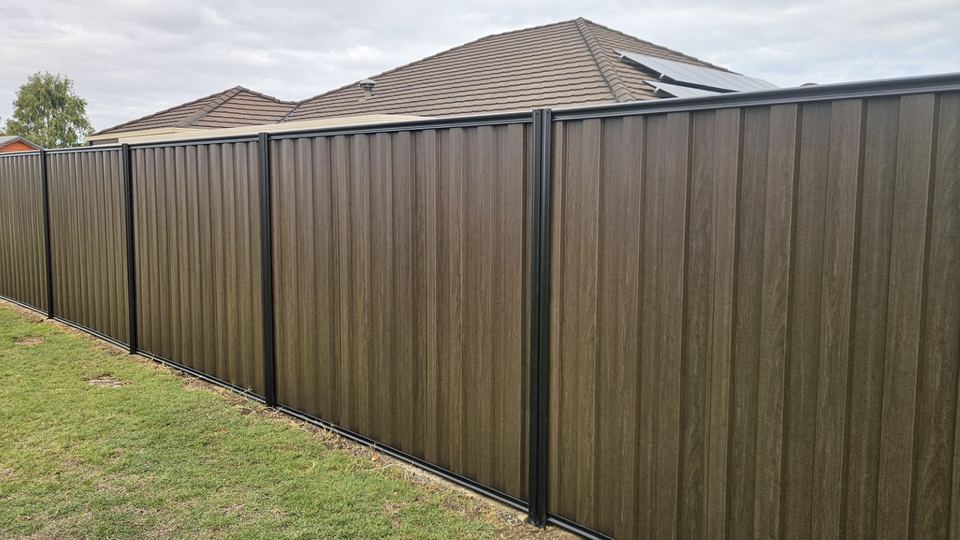 Installed dark brown woodgrain steel fence with black posts and rails along a lawn