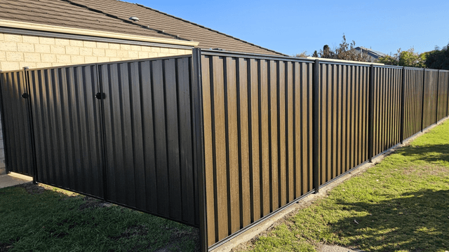 Dark brown woodgrain steel double gates beside a longer run of matching fence
