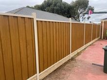 Light Oak woodgrain steel fence with cream posts and rails beside a house