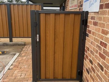 Light Oak woodgrain steel pedestrian gate beside brick